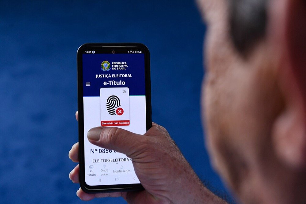 Eleitor segurando celular com o aplicativo e-Título aberto