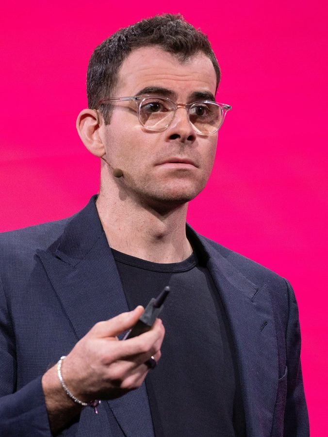 Adam Mosseri, chefe do Instagram, de óculos e blazer escuro, falando num palco com fundo rosa