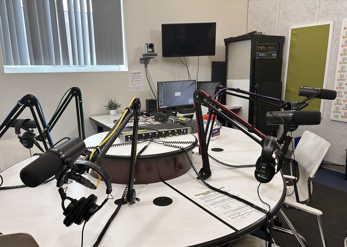 Estúdio de podcast com microfones em braços articulados, fones de ouvido e mesa redonda