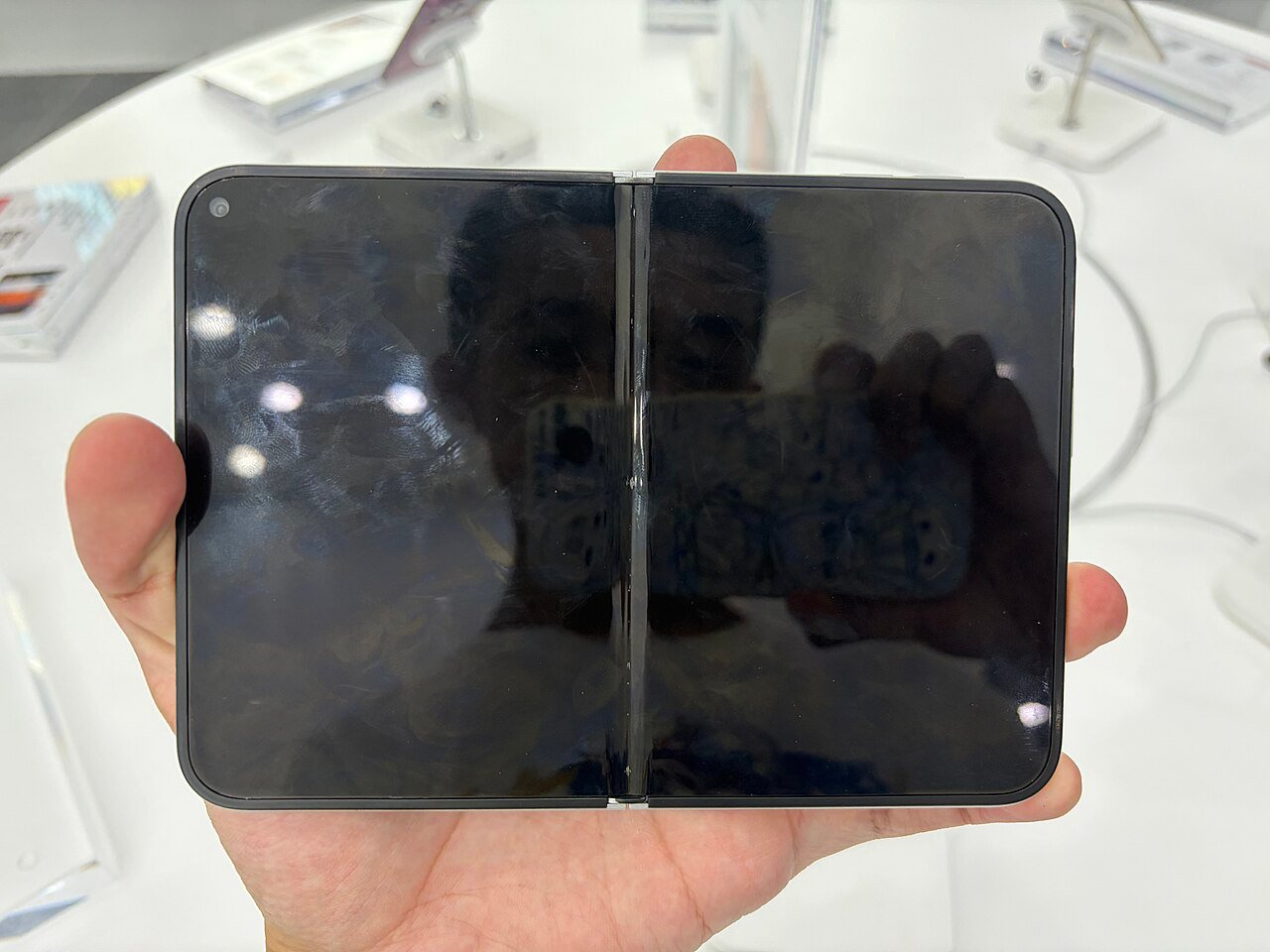 iPhone Duo aberto na mão, com a tela grande desligada e a dobradiça no meio